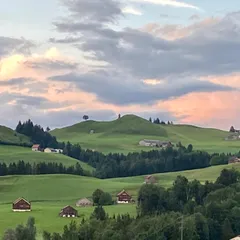 Les collines vertes d'Appenzell au coucher du soleil, avec des granges de bois dans les prairies.