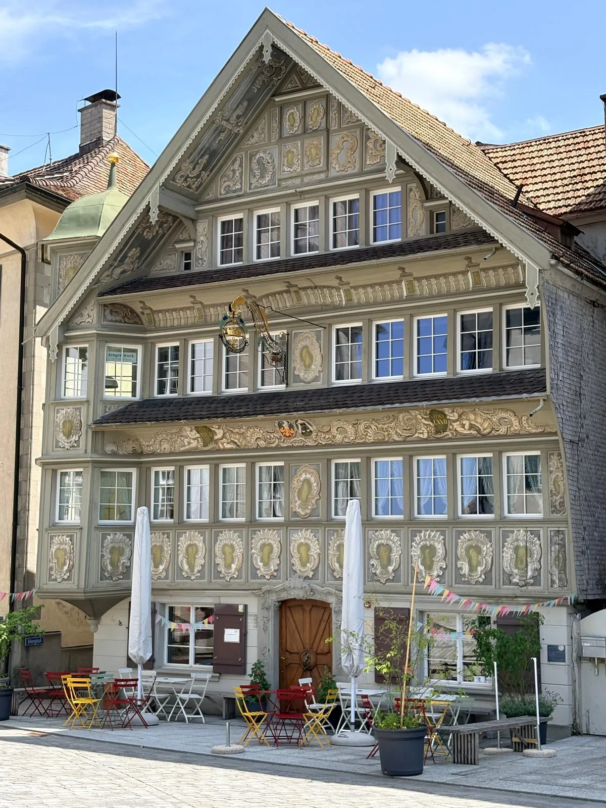 Une maison d'Appenzell à la façade richement peinte, devant une terrasse aux chaises colorées.